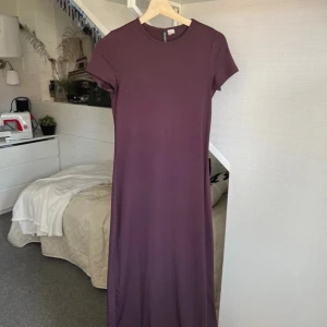 Lång lila klänning med kort ärm - Enkel och stilren långklänning i lila från H&M. Klänningen har rund halsringning och korta ärmar, tillverkad i mjukt och stretchigt material som ger en bekväm passform. Perfekt för dig som gillar minimalistisk stil.