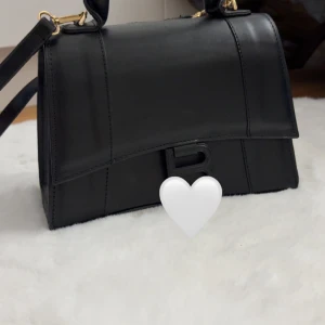 Svart handväska - Säljer en stilren svart handväska med guldfärgade metalldetaljer. Väskan har avtagbar axelrem och ett rymligt fack invändigt. Perfekt för dig som gillar minimalistisk och lyxig design.