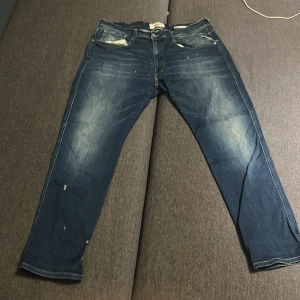 Replay jeans blå, waist 36/30 - Snygga blå jeans från Replay med slitningar och ljusa partier på låren och knäna. Klassisk femficksmodell med raka ben och normal passform. Jeansen är tillverkade i bomull och har detaljerade sömmar på bakfickorna.
