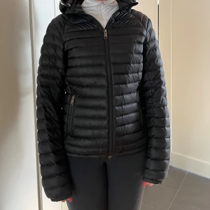 Svart dunjacka Peak Performance - Säljer en svart dunjacka från Peak Performance med huva och dragkedja framtill. Jackan har quiltad design, två fickor med dragkedja och en snygg logga på ärmen. Perfekt för kyliga dagar och riktigt skön att bära. Jackan är i storlek M dam och är i nyskick💕