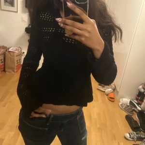 Svart stickad volangtröja - Säljer en svart stickad tröja med volang nertill och hålmönster över hela tröjan. Tröjan har långa ärmar och ribbad kant vid halsen. Perfekt för dig som gillar detaljer och en feminin touch.