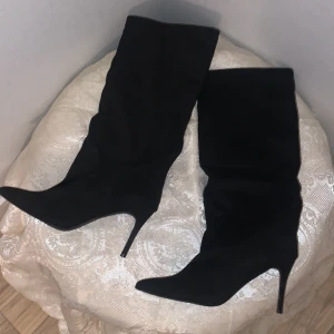 Svarta stövlar/boots - Svart matta stövlar/boots med en smal klack. Lite pösiga upptill i passformen. Helt oanvända i nytt skick. Storlek 39 och har ingen dragkedja. Längden på stövlarna är upp till under knät. Det är lättare att ta på sig skorna försiktigt med hjälp av skohorn. Ser ut att inte tåla vatten.