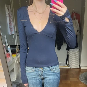 Mörkblå långärmad topp med v-ringning - Säljer en mörkblå långärmad topp med djup v-ringning och tumhål i ärmsluten. Toppen har en slim passform och är tillverkad i ett mjukt, stretchigt material som sitter snyggt på kroppen. Perfekt för dig som gillar en enkel men trendig look.