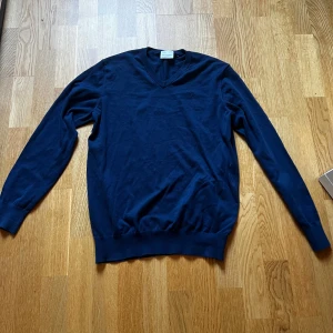 Marinblå v-ringad tröja Peak Performance - Snygg marinblå v-ringad vintage tröja från Peak Performance. Tröjan har lång ärm, diskret broderad logga på bröstet och är tillverkad i mjuk bomull. .