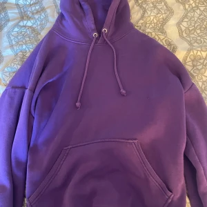 Lila hoodie från BikBok XS - Säljer en lila hoodie från BikBok i storlek XS. Tröjan har huva med snörning och en stor magficka framtill. Perfekt för dig som gillar en chill och enkel stil. Materialet är mjukt och skönt, troligtvis bomull eller polyester.