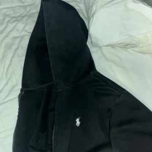 Svart Ralph lauren zip hoodie. - En svart Ralph lauren zip up med utbytt dragkedja. Jag säljer denna eftersom den har blivit för liten för mig, Tröjan är i bra skick förutom att den har en annan dragkedja då den förra gick sönder. Storlek S.