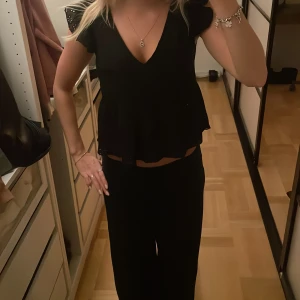 Svart v-ringad blus med volang - Säljer en svart blus med v-ringning och korta ärmar. Toppen har en volangkant nedtill som ger en söt och trendig look. Perfekt att styla med både jeans och kjol för en snygg outfit. Lappen är tyvärr borta så märket är lite oklart heheh 