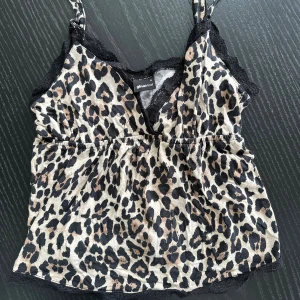 Leopardmönstrad linnetopp Gina Tricot - Säljer en leopardmönstrad linnetopp från Gina Tricot i storlek S. Toppen har tunna axelband, svart spetsdetalj vid halsringningen och nederkant samt en v-ringad front. Färgerna är beige, svart och brun. Perfekt för dig som gillar djurmönster och vill sticka ut.