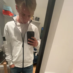 Vit Stone Island zip up tröja - En riktigt fet Stone Island zip up!! Tröjan är i toppen skick, lite skrynklig men det e bara o stryka bort. Köpt här på Plick, för inte alls längesen. Därav inte använd så mycket och fortfarande i ett sjukt bra skick. Jag på bilden är omkring 175 cm, 64 kg. Sitter perfekt bara att den är lite lång i ärmarna. Vid mer info eller bilder är det bara o höra av sig så löser vi det bästa utav det!🤩😊