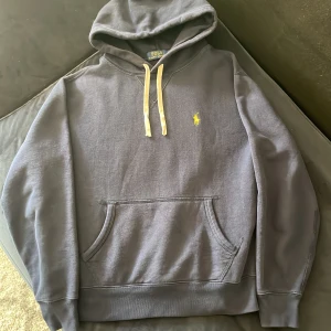Mörkblå Polo Ralph Lauren hoodie  - Säljer en mörkblå hoodie från Polo Ralph Lauren med klassisk gul broderad logga på bröstet. Hoodien är i storlek S men kan passa XS. Perfekt för dig som gillar en clean och stilren look. Om du har något på hjärtat är de bara att fråga. Kan även ta emot byten🤗💯