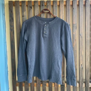 Mörkblå henley KappAhl - Säljer en mörkblå långärmad tröja från KappAhl, Our Best Basics. Tröjan har rund halsringning och knappslå med fyra knappar framtill. Tillverkad i mjuk bomull, perfekt för lager-på-lager och chill dagar.