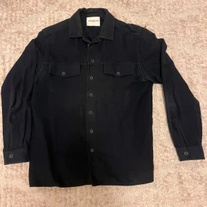 Marinblå overshirt från These Glory Days - Säljer en stilren marinblå overshirt från These Glory Days. Skjortan har klassisk krage, två bröstfickor med lock och knappar hela vägen framtill. Tillverkad i mjuk bomull och passar perfekt till lager-på-lager-stil. Den passar bra på längd för en som är 184 men är för bred.