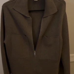 Brun kofta med dragkedja från Åhléns - Säljer en brun kofta från Åhléns Woman i storlek S. Koftan har två stora fickor framtill, klassisk krage och dragkedja hela vägen. Perfekt för lager-på-lager och enkel att matcha med andra plagg.