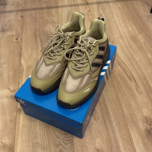 Adidas ZX 2K Boost 2.0 sneakers beige - Adidas ZX 2K Boost 2.0 sneakers i beige och olivgrön med svarta detaljer. Skorna har mesh och syntetmaterial, klassiska tre ränder på sidan och snörning. Snygg chunky sula och modern design, perfekta för dig som gillar streetwear.