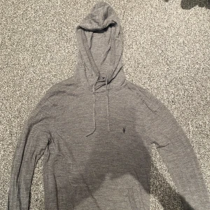 Grå merino hoodie - Säljer en stilren grå hoodie med huva och dragsnören. Perfekt för chill dagar eller när du vill ha en enkel och snygg look.