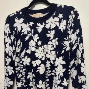 Marinblå blommig långärmat set Michael kors - Supersnyggt marinblått set från Michael Kors med stora vita blommor över hela tyget. Långärmad modell med rund halsringning och rak passform. Perfekt för dig som vill sticka ut med ett fräscht blommönster och klassisk färgkombination.