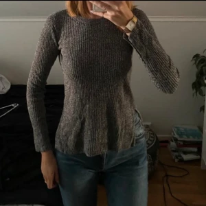 Grå ribbad stickad tröja med slits - Säljer en grå stickad tröja med ribbad struktur och slitsar i sidorna. Tröjan har rund halsringning och långa ärmar, perfekt för lager-på-lager. Snygg till både jeans och kjol.