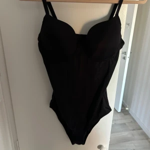 Svart body - Snygg svart body från Nuance med vadderade kupor och justerbara axelband. Klassisk modell med enkel design och diskret knäppning i ryggen. Sitter riktigt bra och ger ett stilrent intryck. Storlek 75C