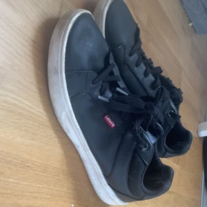 Svarta sneakers från Levi's - Svarta sneakers från Levi's med klassisk design och vit sula. Skorna har snörning och är tillverkade i skinnimitation. Diskret Levi's-logga på sidan ger en clean look. Perfekta för dig som gillar stilrena och bekväma skor.