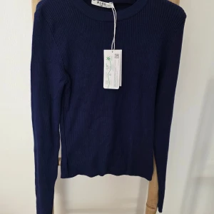 Marinblå ribbad tröja från NA-KD - Säljer en marinblå ribbstickad tröja från NA-KD. Tröjan har rund halsringning och långa ärmar, perfekt för lager-på-lager. Enkel och stilren modell som är lätt att matcha med olika outfits.