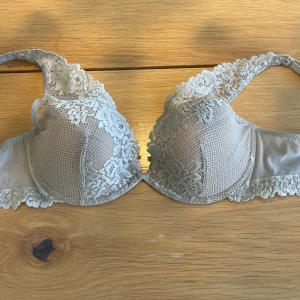 Grå spets-bh Elena 80B Intimissimi - Säljer en snygg bh i isgrå färg från Intimissimi, storlek 80B. Bh:n har vacker spets med blommönster och meshdetaljer över kuporna samt längs axelbanden. Perfekt för dig som gillar en feminin och stilren look. Aldrig använd.