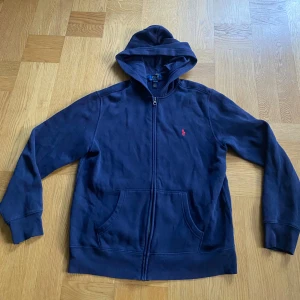 Mörkblå Polo Ralph Lauren - Säljer en mörkblå zip up hoodie från Ralph Lauren. Tröjan är i storlek L(14-16) men passar dig som är mellan 160-170 cm. Den är i bra skick och har inga hål eller fläckar