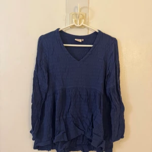Blå v-ringad blus med volang - Säljer en blå blus med v-ringning och långa ärmar. Blusen har en luftig passform, volangdetaljer nedtill och ett diskret strukturerat tyg. Perfekt för dig som gillar en avslappnad men ändå stilsäker look. Storlek S men passar nog bättre på m eller l!!💕🥰