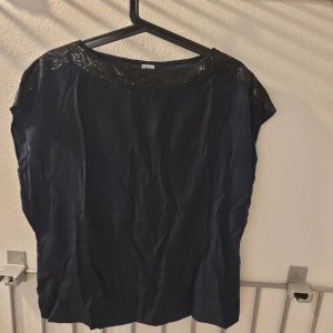 Mörkblå blus med paljettdetalj Saint Tropez - Snygg mörkblå blus från Saint Tropez med glittrande paljetter längs halsringningen. Blusen har en lös passform och är ärmlös, perfekt för att lyfta din outfit med lite extra bling. Materialet känns mjukt och följsamt.