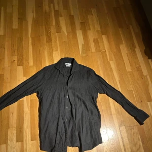 Svart linneskjorta från Massimo Dutti - Stilren svart skjorta från Massimo Dutti i 100% linne. Skjortan har klassisk krage, knäppning framtill och långa ärmar. Perfekt för dig som gillar en avslappnad men ändå snygg look.