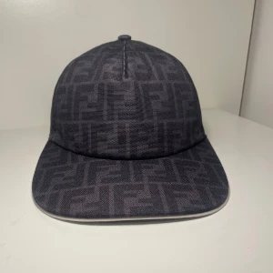 Svart keps från Fendi med FF-mönster - Snygg svart keps från Fendi med ikoniskt FF-logomönster över hela kepsen. Klassisk böjd skärm med vit kant och justerbar rem baktill. Tryck på köp så är denna härliga keps påväg till dig inom 6 timmar. Skriv om du har minsta lilla fråga! 