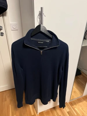 Marinblå half zip tröja Jack & Jones - Snygg marinblå långärmad tröja från Jack & Jones med half zip-dragkedja vid kragen. Tröjan har en klassisk, stilren look och är tillverkad i mjukt material som känns skönt mot huden. Perfekt för dig som gillar enkel och clean stil. Storlek M, inga defekter eller sådant!