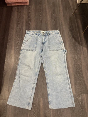 Ljusblå cargopants från Gina Tricot  - Ljusblå cargopants i jeansmaterial från Gina Tricot. Byxorna har raka, vida ben, stora fickor fram och bak samt en extra ficka på sidan. Perfekt för dig som gillar en avslappnad och trendig look.