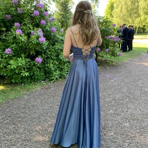 Blå långklänning i satin med snörning - Säljer en elegant blå långklänning i glansigt satinmaterial. Klänningen har smala axelband, v-ringning och öppen rygg med snygg snörning. Kjolen är vid och har fickor, vilket är superpraktiskt. Perfekt för bal eller student! Klänningen är uppsydd för att passa min längd, jag är 161 men klänningen var lång på mig och hade klacka. Nypris var 4000