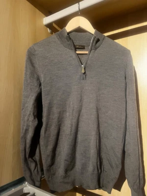Grå/grön stickad half zip från Stenströms - Säljer en stilren grå stickad tröja från Stenströms med half zip och ribbade muddar. Perfekt till lager på lager och har en klassisk passform med lång ärm och hög krage. Enkel att matcha till olika outfits. Färgen är grå/grön.