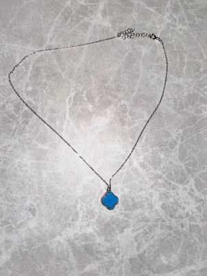 Silverhalsband 925 med blått klöverhänge - Säljer ett fint halsband i äkta silver (925) med blått klöverformat hänge. I gott skick. Passar både till vardag och fest.