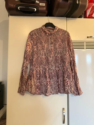 Mönstrad rosa och vinröd skjorta - Säljer en långärmad skjorta med unikt mönster i rosa och vinröda toner. Skjortan har knappar framtill, klassisk krage och ett flowy fall nedtill. Materialet känns lätt och luftigt, perfekt för dig som gillar statement-plagg med coola detaljer. Från märket Odd Molly. Storlek 3 som enligt deras storleksguide motsvarar en L. Mycket fint skick, jag hittar inga synliga anmärkningar eller defekter. 