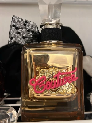 Juicy Couture gold parfym - En statement-parfym från Juicy Couture med coolt guld- och rosa detaljer samt en svart rosett. Perfekt för dig som vill sticka ut och addera lite glamour till din stil 100 ml, helt full, bara testad 1 gång.