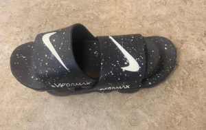 Nike Vapormax svarta sandaler - Svarta Nike Vapormax sandaler med vit swoosh och coolt stänkmönster över hela ovandelen. Sulan är tjock och har en unik, vågig design som ger extra komfort. Tillverkade i syntetmaterial och har öppen tå för chill vibe. Perfekt för sommardagar när du vill sticka ut.
