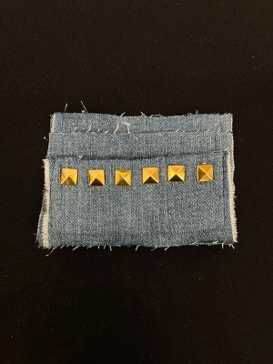 Plånbok i denim med nitar - Plånbok i ljusblå denim med råa kanter och sex guldiga fyrkantiga nitar på framsidan. Perfekt för dig som gillar en edgy och unik stil. Enkel och kompakt design som får plats i fickan eller väskan.