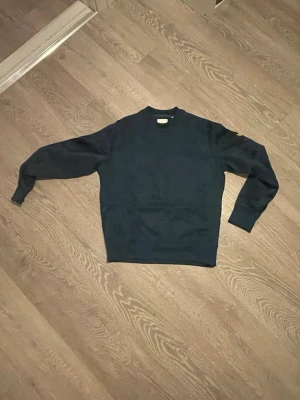 Mörkblå sweatshirt från Lyle & Scott - Mörkgrön sweatshirt från Lyle & Scott i relaxed fit. Tröjan har rund hals, långa ärmar och klassisk logga med gul fågel på vänster ärm. Tillverkad i mjuk bomull, perfekt för en chill och stilren look.