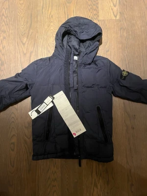 Mörkblå dunjacka från Stone Island - Snygg äkta mörkblå dunjacka från Stone Island, köpt på NK Göteborg har kvitto och prislapp. Anledning till att jag säljer den till detta pris är att jag köpte den på 50% rabatt