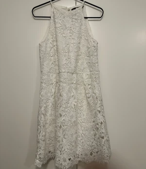 Vit spetsklänning från Zara - Supersöt vit kortklänning från Zara Basic i storlek XS. Klänningen har ett blommigt spetsmönster, hög hals och knytning i nacken. Fodrad under och med en lätt utställd kjol. Perfekt för sommarens alla tillfällen!