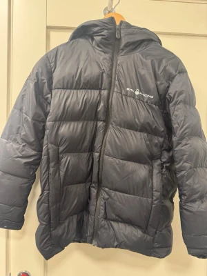 Svart dunjacka från Sail Racing - Svart dunjacka från Sail Racing med huva.Fylld med 80/20 dun och fjäder, 600 fill power. I använt skick. Två små hål som är lappade, se bilder. 