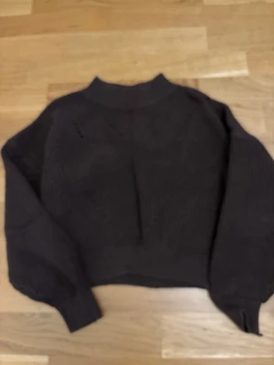 Brun stickad tröja från H&M - Mysig brun stickad tröja från H&M med hög hals och breda, långa ärmar. Tröjan har en ribbad struktur och är perfekt för kyligare dagar. Enkel och stilren design som passar till det mesta.