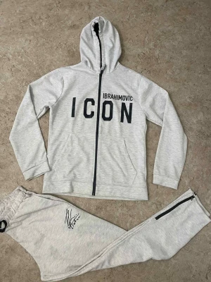 Grå mjukisbyxor Dsquared2 ICON - Snygga grå mjukisbyxor från Dsquared2 ICON med svart dragkedja vid benslut och elastisk midja med snörning. Byxorna har en cool Ibrahimovic-autograf tryckt på benet och är gjorda i mjukt bomullsmaterial. Perfekt för chill och sportig stil.