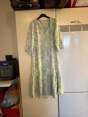 Lång blommig klänning från Cream - Luftig långklänning från Cream i storlek 38 med v-ringning och trekvartsärmar. Klänningen har ett blommigt mönster i ljusblått, grönt och vitt, samt volangdetaljer nertill. Perfekt för vår och sommar med sitt tunna, sköna material. Storlek 38. Mycket fint skick, jag hittar inga synliga anmärkningar eller defekter. 