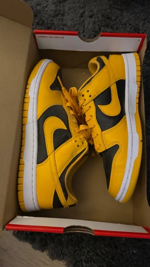 Nike Dunk Low Retro svart/gul EUR 42 - Nike Dunk Low Retro sneakers i svart och gul (goldenrod) med vit mellansula. Klassisk låg modell med snörning och rund tå. Ovandel i skinn och slitstark gummisula. Perfekt för dig som vill sticka ut med färg på fötterna.  Nypris: 1800, nyskick.