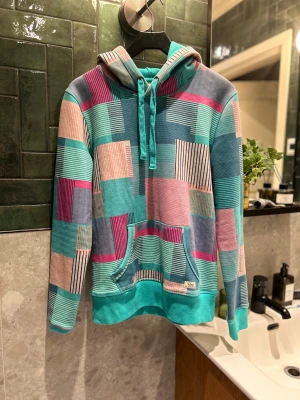 Roxy färgglad patchwork hoodie – stl M - Unik och färgstark hoodie från Roxy i patchwork-stil med turkost, rosa, beige och marinblått. Mjuk insida och känguruficka fram. Storlek M, passar både oversized och normalt beroende på kroppstyp. I fint skick och väldigt ovanlig design.