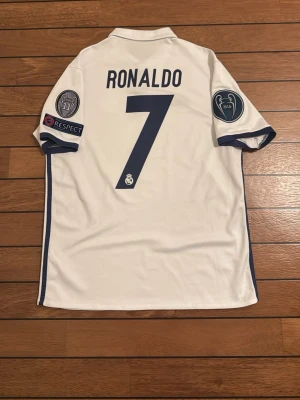 Ronaldo 2016/17 Hemmatröja – Real Madrid Champions League  -  Fin tröja från säsongen 2016/17 med Ronaldo på ryggen och CL-badges på ärmarna. Perfekt för samlare eller fans.
