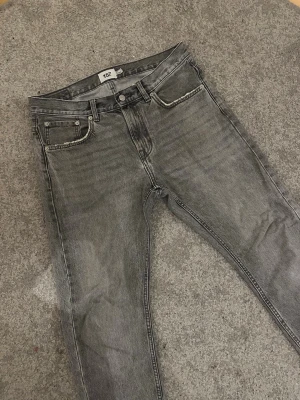 Grå jeans från 157, straight fit - Snygga grå jeans från 157 med klassisk femficksdesign och raka ben. Jeansen har en mörkgrå tvättad look, normal passform och midwaist. Materialet är robust denim och de har detaljer som knappar och dragkedja framtill. Snygga slitningar på fickor och vid vristen. Modellen är 183 och väger 72kg, strl: W30, L32. Pris kan diskuteras.